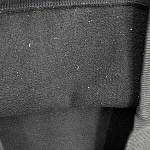 May include: Close-up of a black fabric with a textured surface. The fabric has small white specks scattered across it. The top edge of the fabric is a darker black, and the right edge has a ribbed texture.