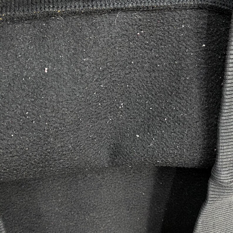May include: Close-up of a black fabric with a textured surface. The fabric has small white specks scattered across it. The top edge of the fabric is a darker black, and the right edge has a ribbed texture.