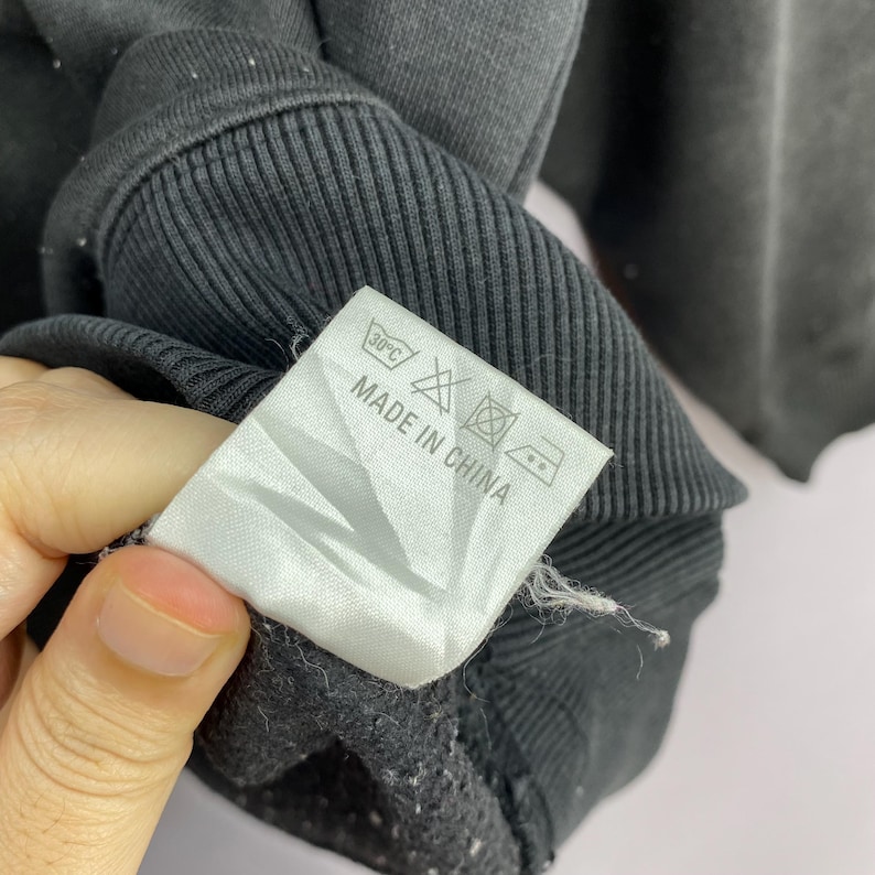 May include: Close-up of a black sweatshirt with a ribbed collar and cuffs. A white tag with washing instructions and the text "MADE IN CHINA" is visible.