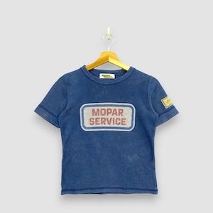 May include: A blue short-sleeve t-shirt featuring a rectangular graphic on the chest with the text MOPAR SERVICE in red letters. The shirt has a small yellow patch on the left sleeve and a yellow brand label inside the collar, hanging on a hanger.