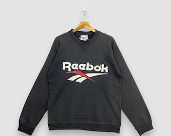 Sudadera Reebok vintage de los 90, negra, con cuello redondo y costuras en V, logo clásico vectorial, estilo jersey deportivo, talla 3XL.