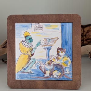 Op de afbeelding: Vierkante keramische tegel met een handgeschilderde illustratie van een figuur in gele gewaden die twee katachtige wezens lesgeeft. De tegel is geplaatst in een donkerbruine houten lijst. De tekst "EV SOV OMESTRE DACOLFA" is zichtbaar.