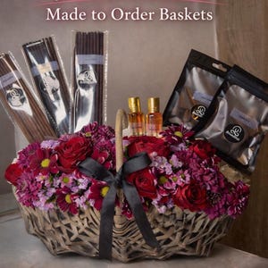 May include: A Valentine's Day gift basket filled with fresh flowers, incense, perfume oils, and bakhoor. The basket is decorated with a black ribbon and contains a variety of products. Text on the image reads "Valentine's Made to Order Baskets."