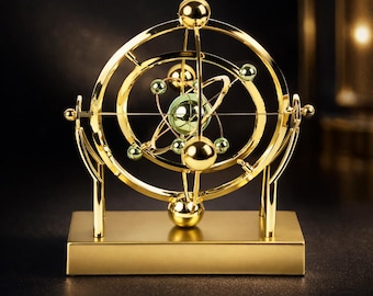 Op de afbeelding: Een goudkleurige, kinetische sculptuur die een orbitale model van het zonnestelsel uitbeeldt. De sculptuur heeft meerdere cirkelvormige ringen, bollen en een centrale globe, allemaal gemonteerd op een rechthoekige basis. Het ontwerp is ingewikkeld en gedetailleerd, met een gepolijste afwerking.