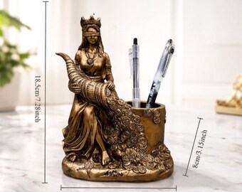 Op de afbeelding: Een bronzen pennenhouder met een zittende figuur met een blinddoek en kroon, die een hoorn des overvloeds vasthoudt. De pennenhouder is 18,5 cm hoog, 13,5 cm breed en 8 cm diep. Er zitten twee pennen in.