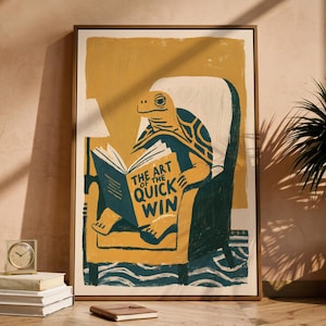 May include: A framed wall art print featuring a stylised illustration of a turtle sitting in a dark teal armchair, reading a book titled The Art of the Quick Win. The artwork uses a colour palette of mustard yellow, dark teal, and cream, with a textured finish.