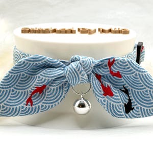 May include: A blue and white patterned cat collar with a bow tie design. The collar features a wave pattern with red and black koi fish. A silver bell hangs from the collar. The text "Sweetie Pie" is visible on the top.