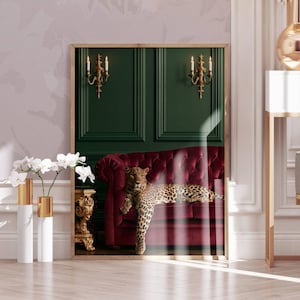 Peut inclure: Une impression d'art encadrée représentant un léopard allongé sur un canapé en velours capitonné rouge profond. Le fond se compose de murs vert foncé à panneaux ornés de deux appliques murales dorées. La scène dépeint un intérieur luxueux.