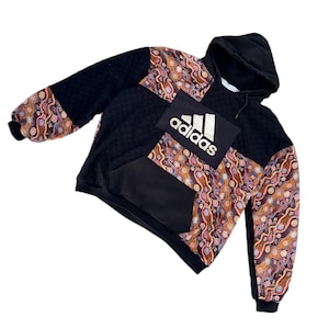 May include: Black hoodie with a kangaroo pocket and hood. The sleeves and upper chest have a colourful pattern in orange, brown, and cream. The Adidas logo is displayed on the front.