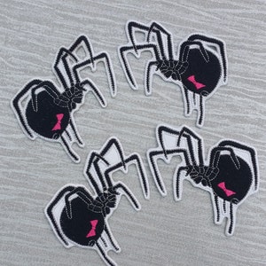 Peut inclure: Quatre patchs d'araignées noires avec des contours blancs et des nœuds roses. Les araignées sont disposées en cercle sur une surface grise.