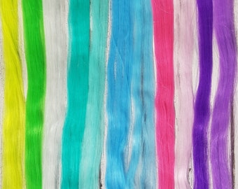 May include: Eight strands of colorful synthetic hair extensions. The colors are neon green, white, turquoise, light blue, pink, lavender, and purple. The hair extensions are about 20 inches long.