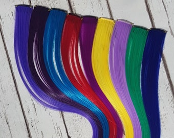 May include: A set of ten colorful hair extensions with clips. The colors are purple, blue, teal, red, magenta, yellow, lavender, green, and dark blue. The hair extensions are arranged in a rainbow pattern.