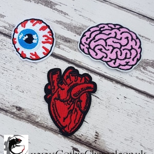 May include: Three embroidered iron-on patches: a red heart, a pink brain, and a white eyeball with a blue iris and red veins.