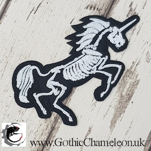 May include: White embroidered skeleton unicorn patch on a black background. The unicorn is standing on its hind legs with its horn pointing up.
