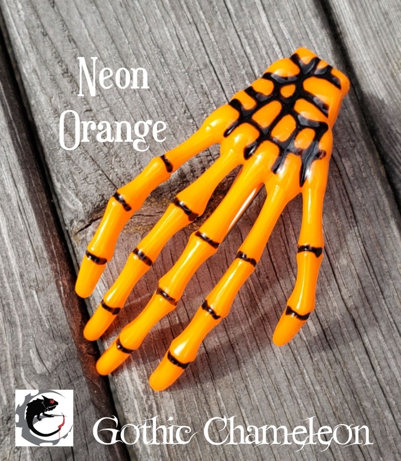 May include: Neon orange skeleton hand hair clip. The hand is made of plastic and has black details.