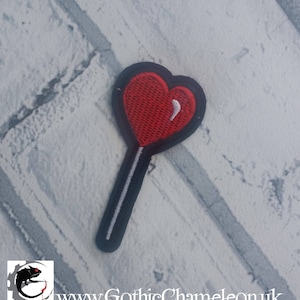 Puede incluir: Parche bordado de lollipop en forma de corazón rojo con un palo negro y blanco.