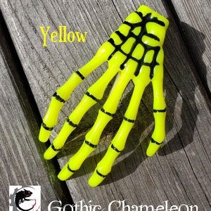 May include: Yellow skeleton hand hair clip. The hand is made of plastic and has black details. The text "Yellow" is visible in the image.