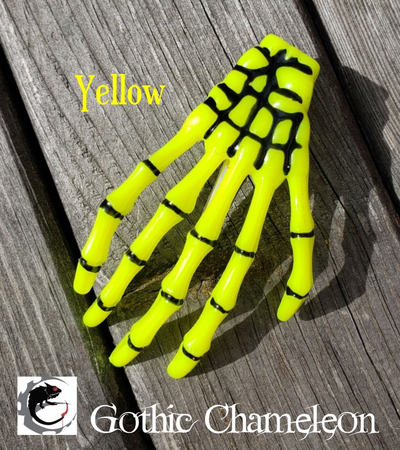May include: Yellow skeleton hand hair clip. The hand is made of plastic and has black details. The text "Yellow" is visible in the image.