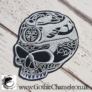 May include: A black and white embroidered skull patch with a Celtic knot design. The skull is outlined in white and the knot design is in silver thread.