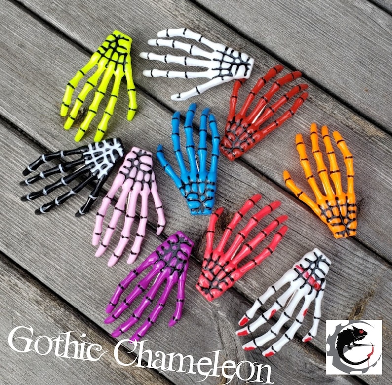 May include: A set of ten skeleton hand hair clips in various colors, including yellow, white, blue, red, orange, pink, and purple. The clips are made of plastic and have a black spiderweb design.