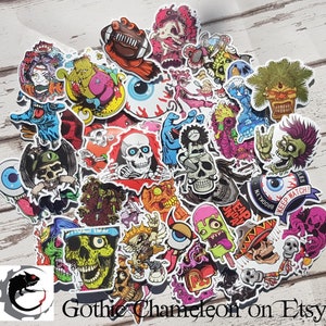 May include: A collection of colorful stickers featuring various spooky and grotesque designs. The stickers include skulls, zombies, eyeballs, and other horror-themed illustrations. The text "Gothic Chameleon on Etsy" is visible.