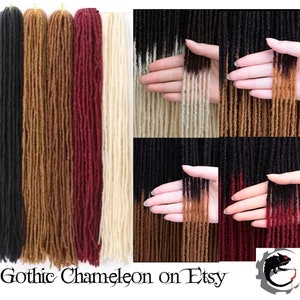 May include: Five bundles of synthetic dreadlocks in various colors, including black, brown, burgundy, and blonde. Each bundle is ombre, with a darker color at the roots and a lighter color at the ends. The dreadlocks are displayed on a white background.