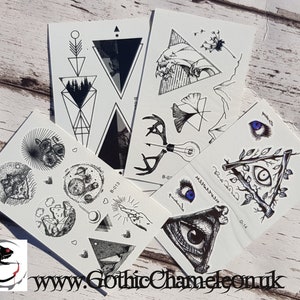 May include: Set of eight black and white temporary tattoos with various designs, including a deer head, a wave, a tree, an eye, and geometric shapes. The tattoos are printed on white paper and have a glossy finish.