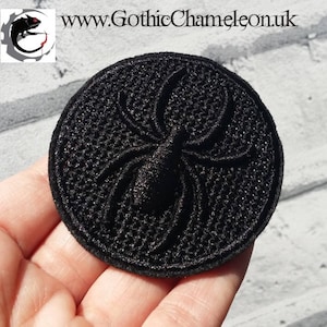 Op de afbeelding: Zwarte geborduurde spin-patch met een spinnenweb-ontwerp. De patch is rond en heeft een zwarte achtergrond.