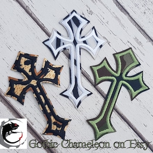 May include: Three iron-on patches in the shape of crosses. The crosses are in different patterns: black and tan, white and black, and green and black.