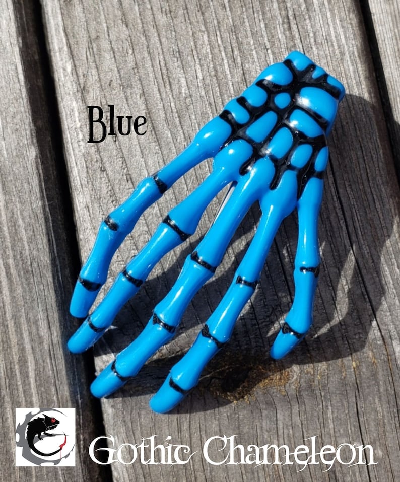 May include: Blue skeleton hand hair clip with black detailing.  The clip is made of plastic and has a shiny finish.