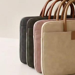 May include: A row of laptop bags in various colors: dark gray, olive green, pale pink, and beige. Each bag has a matching handle and a front pocket. The handles are brown.