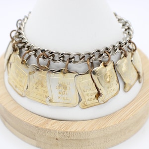 May include: A silver-toned metal charm bracelet featuring multiple rectangular gold-toned charms. Each charm is engraved with a commandment, including text such as 'THOU SHALT NOT KILL' and 'THOU SHALT NOT COMMIT ADULTERY', suspended by small metal rings.