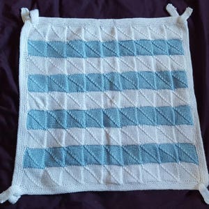 May include: A white knitted baby blanket with blue stripes. The blanket is made of a soft, textured yarn and has a simple, geometric design.