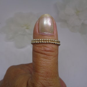 May include: A gold beaded ring with two rows of beads. The ring is worn on a person's thumb.
