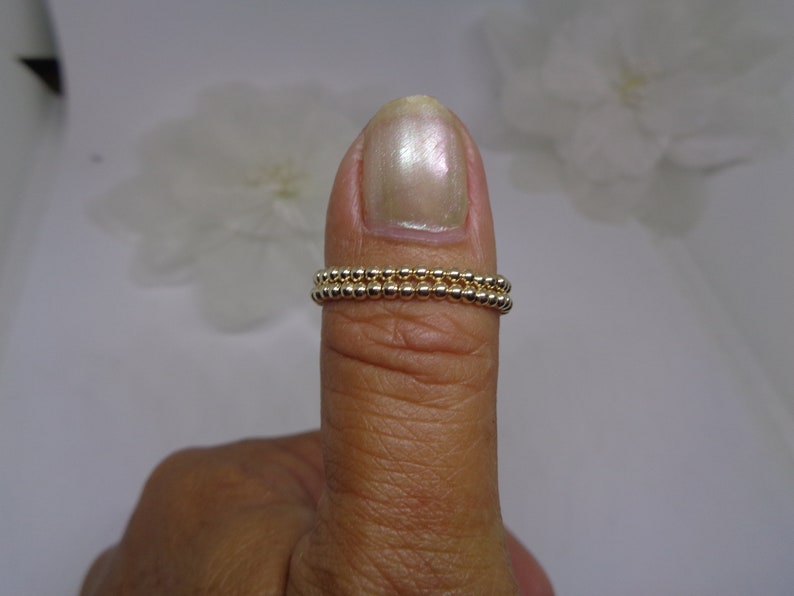 May include: A gold beaded ring with two rows of beads. The ring is worn on a person's thumb.