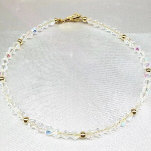 May include: A delicate bracelet featuring clear, faceted crystals and small gold-colored beads. The bracelet is strung on a thin, gold-toned chain and has a gold-colored clasp. The crystals catch the light, creating a sparkling effect.