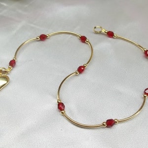 May include: A gold anklet with a heart charm and red beads.