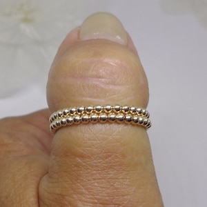 May include: Two gold beaded rings stacked on a finger. The rings are made of small, round beads.