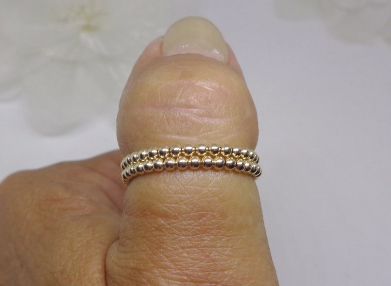 May include: Two gold beaded rings stacked on a finger. The rings are made of small, round beads.