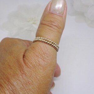 May include: A gold beaded ring worn on a thumb. The ring is made of two rows of small, round beads.