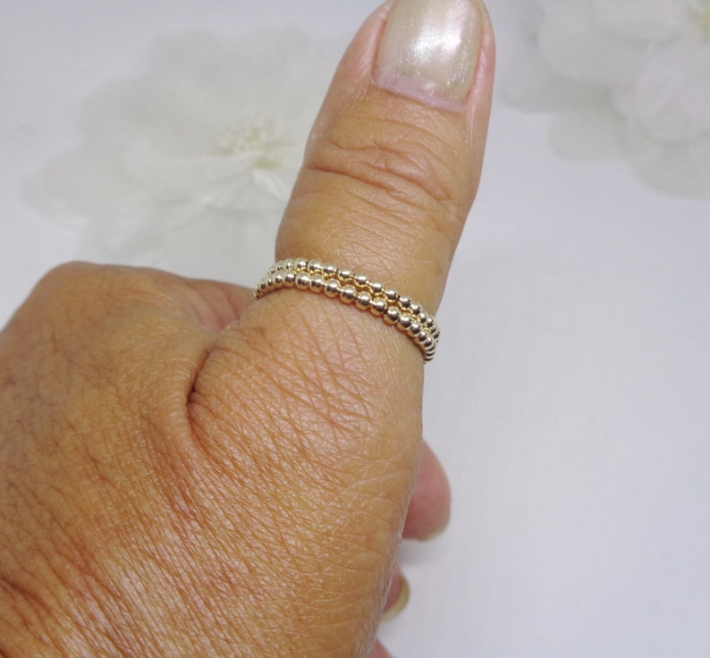 May include: A gold beaded ring worn on a thumb. The ring is made of two rows of small, round beads.