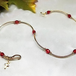 May include: Two gold bracelets with red beads and a small cross charm. The bracelets are delicate and simple, perfect for everyday wear.