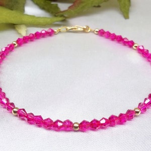 May include: A pink crystal bracelet with gold beads. The bracelet is made of small, faceted crystals that are strung together on a gold chain.