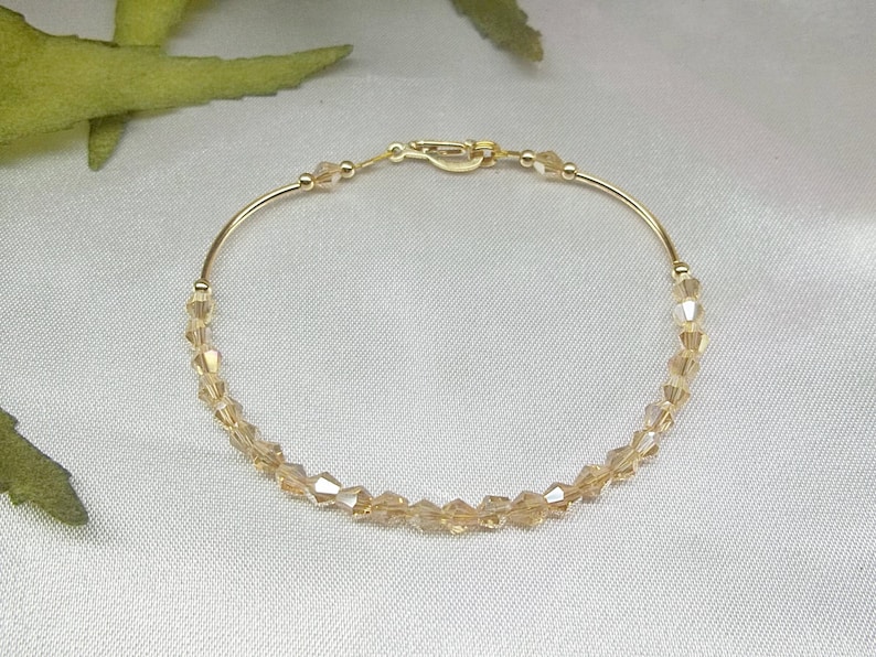 Op de afbeelding: Een gouden armband met een delicate ketting en heldere kristallen kralen.