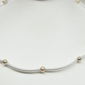 May include: A silver necklace with gold beads. The necklace is on a white surface.