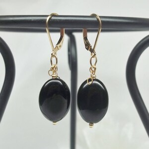 May include: A pair of gold dangle earrings with black oval-shaped gemstones.