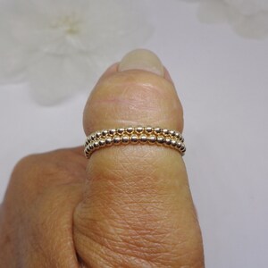 May include: Two gold beaded rings stacked on a finger. The rings are made of small, round beads.