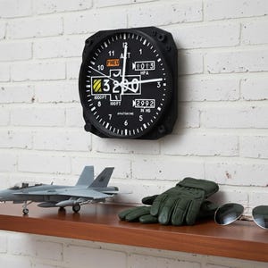 May include: Aviation-themed decor featuring a black altimeter clock on a white brick wall. Below, a model airplane, green gloves, and sunglasses rest on a wooden shelf. The clock displays numbers and text, including "1000FT" and "2992 IN HG".