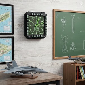Fighter jet pilot wall clock in the style of a MFD (multi function display). Square black housing with light grey buttons and green lcd displaying time.