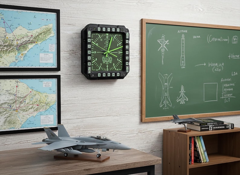 Fighter jet pilot wall clock in the style of a MFD (multi function display). Square black housing with light grey buttons and green lcd displaying time.
